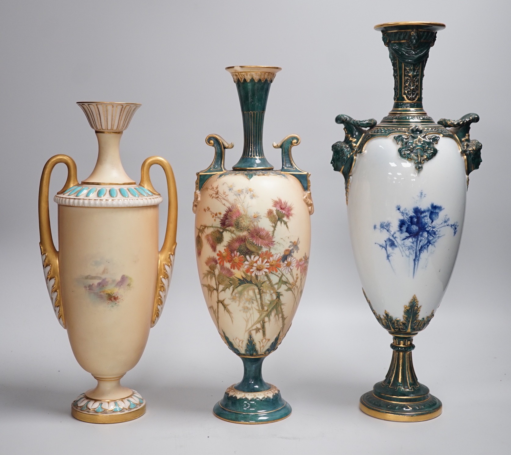 Three Royal Worcester pedestal vases, each of ovoid form and supported on circular pedestal feet, two are decorated with flowers and thistles, the other depicting a rural landscape within a gilt foliate C scroll cartouch